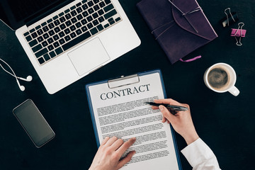 cropped shot of businesswoman signing contract at workplace isolated on black