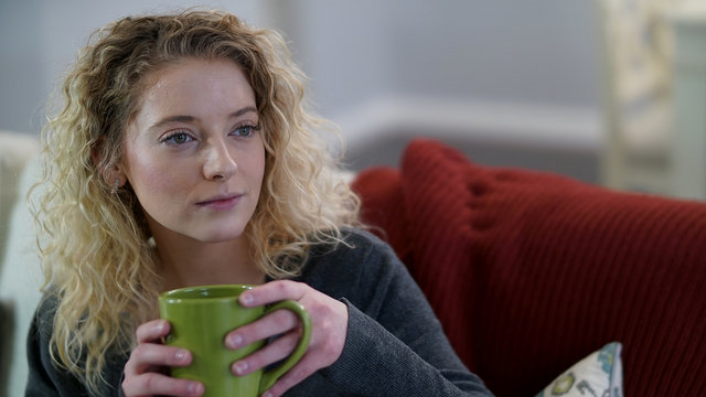 Attractive blonde woman sitting with green coffee cup looking to the right