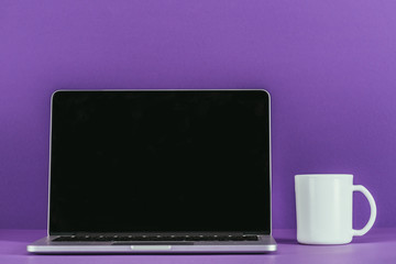business workplace with laptop and coffee mug on purple surface