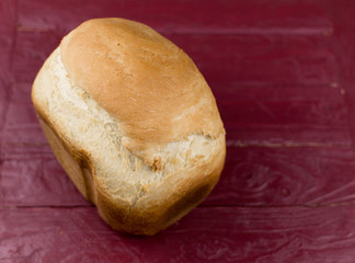 A loaf of homemade white bread on a dark red wooden background.
