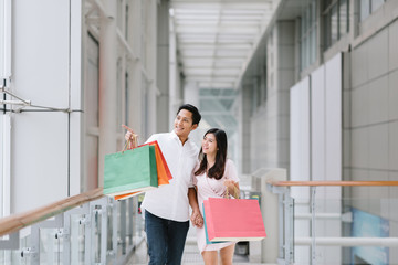 Happy Asian couple holding colorful shopping bags and enjoying shopping, having fun together in mall. Consumerism, love, dating, lifestyle concept © interstid