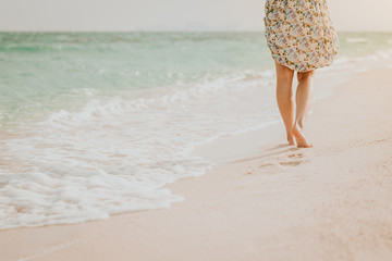 woman walking on beach leaving footprints in the sand during sunset