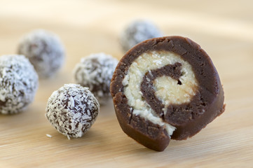 chocolate coconut balls and roulade decorated with shredded coconut on wooden bamboo table