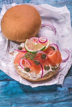 Burger with cream cheese, smoked salmon, red onion, capers and lemon on rustic blue table