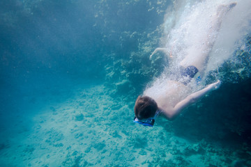 Boy in swimming mask diving in Red sea near coral reef
