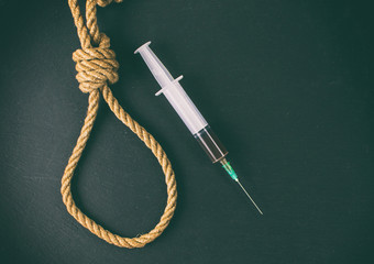 Drugs are suicide. A hinge for the gallows and a syringe with heroin on a black background.