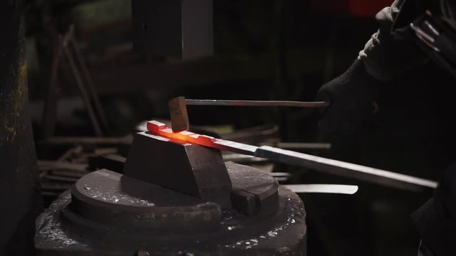 close up shot of a blacksmith's hands, a man hits the hammer with a hammer over a hot piece of steel, which will then become a horseshoe, the person is in a blacksmith shop