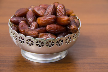 Dates fruit on a silver bowl on wooden table. The Muslim feast of the holy month of Ramadan Kareem