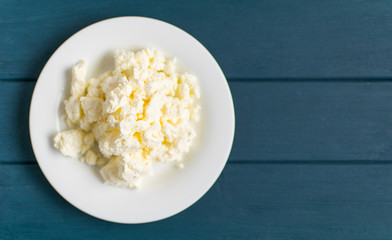 Cottage cheese on a white plate on a blue wooden background.
