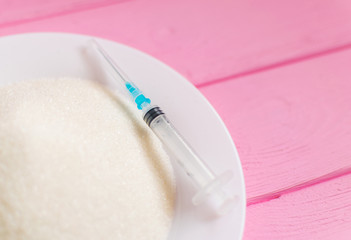 Sugar and a syringe in a plate on a pink background. The concept of possible harm from sugar.