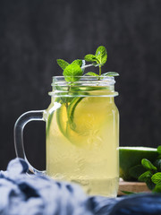 Cold beverage mojito in a glass jar with lime and mint on a table against black wall.