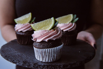 Tasty cupcakes on background table. Homemade chocolate muffin cupcake with cream buttercream icing. Birthday cupcake. Valentine cupcake sweets. Close up woman hands holding cupcakes
