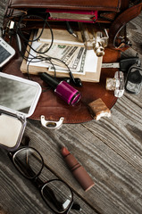 women's things scattered from the bag on wooden boards.
