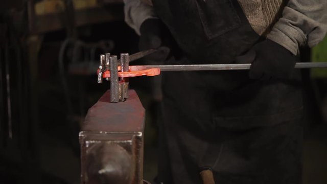 close up shot of a blacksmith's hands, a man holding a hot piece of steel and bending it with tools to create a horseshoe for horses, a professional working on an anvil