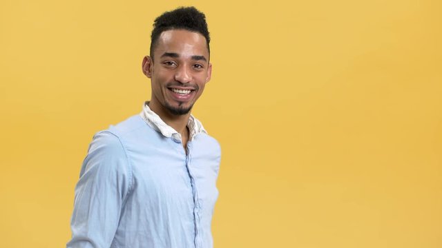 Portrait of smiling arabic guy with beard and mustache showing OK or alright sign on camera, isolated over yellow background. Concept of emotions