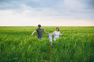 Joyful man, woman walk on green field background, rest, have fun, play, run with little cute child baby boy. Mother, father, little kid son. Family day 15 of may, love, parents, children concept.