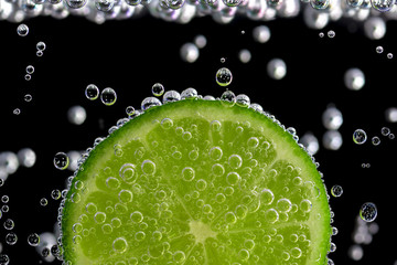 A slice of lime in soda water on a black background. 
