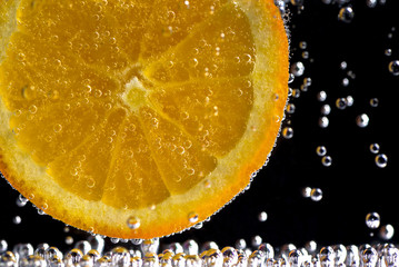 Fototapety  Plasterek pomarańczy w wodzie sodowej na czarnym tle.