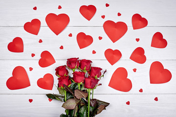 Top view of bouquet red roses and paper hearts on white wooden background, copy space. Greeting card mockup for Saint Valentines Day, Womens Day (March 8), Mothers Day. Love, wedding concept, flat lay