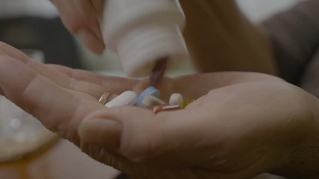 Grandmother emptying a bottle of supplements and vitamins in her hand swallowing them with a glass of water at home