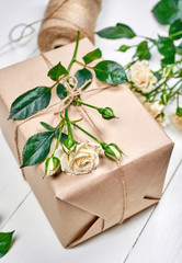 Fototapeta na wymiar Gift box with branch of fresh roses on wooden table, copy space. Holiday background, sale, shopping. Gift wrapping. Greeting card for Valentines Day, Womens Day, Mothers Day, flat lay