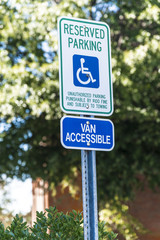 Vertical shot of a handicapped parking sign with a 15 mile per hour sign below it.  Out of focus trees and a building in the background.