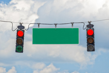 Horizontal shot of two red traffic lights hanging from a cable with a blank street sign in-between...