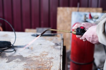 A man welds a metal with a gas burner