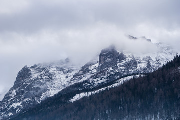 Dramatic alpine scenery with fog and clouds shrouding the mountain top while forests cover the slopes