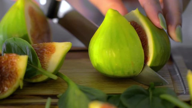 Close-up shot of cutting green fig on wooden board with basil leaves. View to fruit cut in warm sunlight