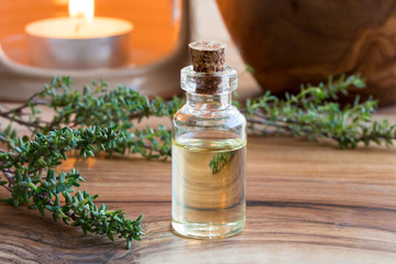 A bottle of thyme essential oil with fresh thyme twigs and an aroma lamp