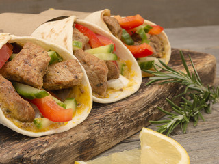 Fresh tortilla with pork meat and fresh vegetables on wooden board. 