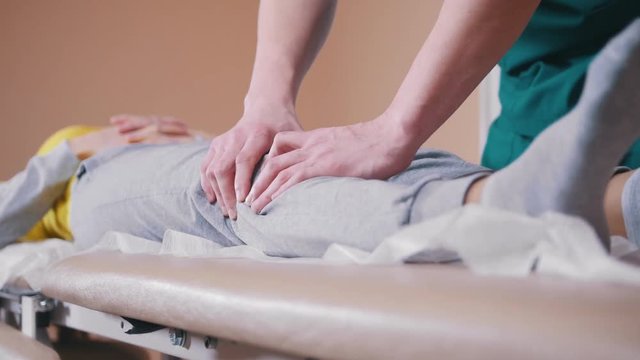Manual therapist massaging a young woman lying on a massage table, stretching her knees