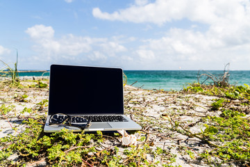 A laptop and a pair of reading glasses at the tropical beach. Working holiday concept.