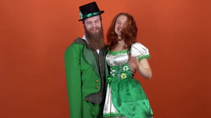 Young couple in costumes celebrating saint patrick's day isolated on orange wall embrace