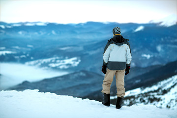 Fototapeta na wymiar the guy is standing on top of a snowy mountain looking into the distance, the view from behind