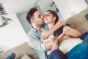 Tender smiling couple with digital tablet sitting on sofa at home