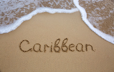 Word Caribbean written on the sand near the sea.
