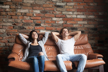 Obraz premium Young happy couple relaxing on comfortable leather couch at home, relaxed smiling man and woman resting on sofa in loft interior breathing fresh air meditating together, no stress, positive thinking