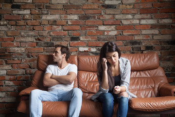 Obraz premium Frustrated upset couple in quarrel not talking after fight, offended stubborn insulted jealous man sitting silent on sofa at home with sad depressed disappointed woman, marriage relationships problem