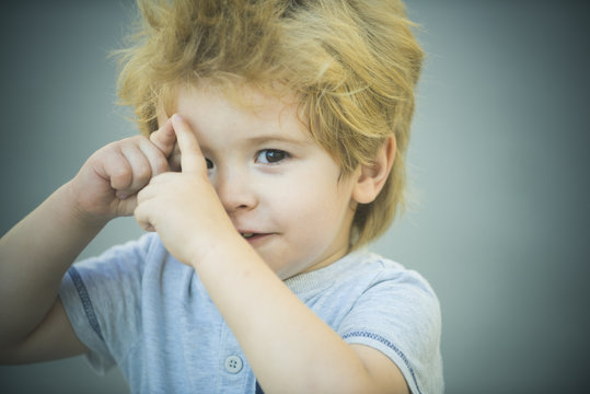 Boy Makes Fun Hands Gestures, Isolated On Gray Background. Adorable Blond Toddler Plays With Hands And Smiles To Camera. Cunning Little Boy. Smart Child's Clever Look. Funny Boy 3 Years Old Portrait