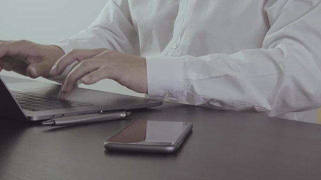 Businessman hand working with mobile phone and laptop in modern office in slow motion
