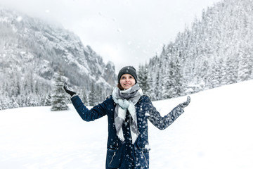 Uśmiechnięta dziewczyna rzuca śniegiem w górach zimą.