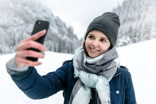Uśmiechnięta dziewczyna robi sobie selfie w g&oacute;rach zimą.