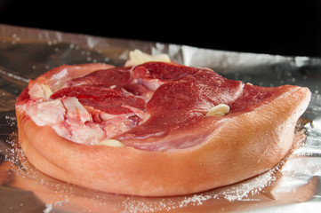 A raw piece of meat is sprinkled with sea salt, pepper. Foil for baking