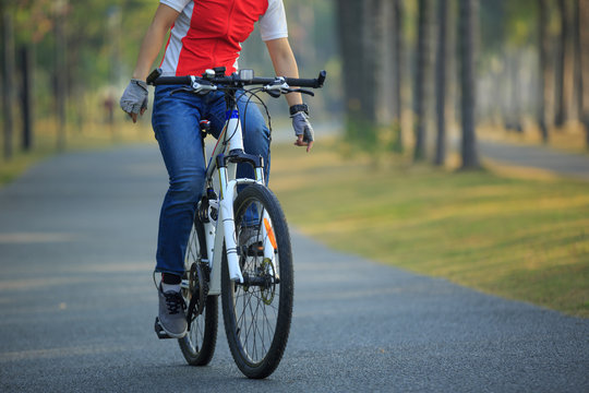 Woman cyclist riding bike with outstretched arms in tropical park