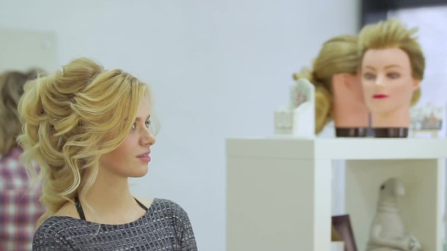 Cute blonde girl admires herself in the mirror in the beauty salon. Close up