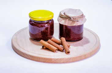 Glass jars of strawberry jam and cinnamon sticks on wooden plate
