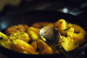 Roasted potatoes close up in a fragrant seasoning in a pan in a spoon