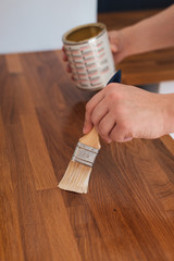 Close up of man's hand applying linseed wood treatment oil with paint brush for protection against water on wooden oak kitchen counter surface after sanding with sanding paper
